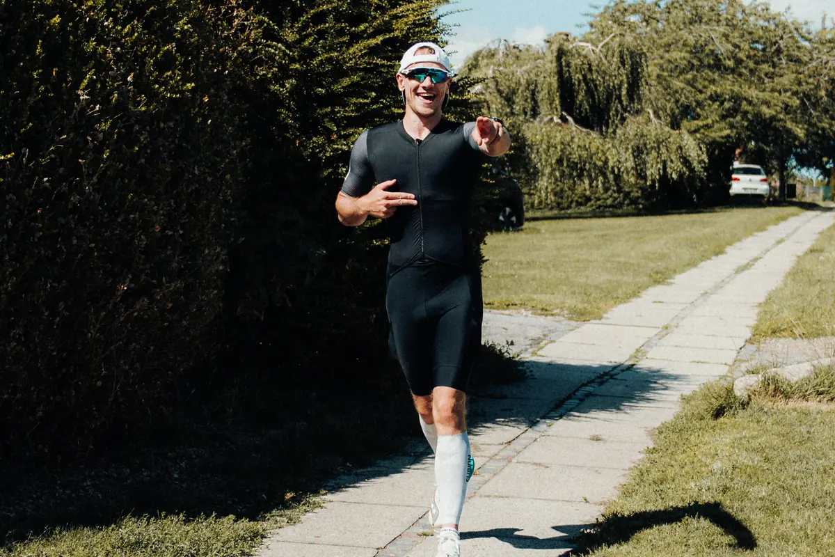Duathlon – løber i trisuit på løbetur - Coach Lykke Endurance Duathlon: smilende løber i sort trisuit løber på en sti i solskin