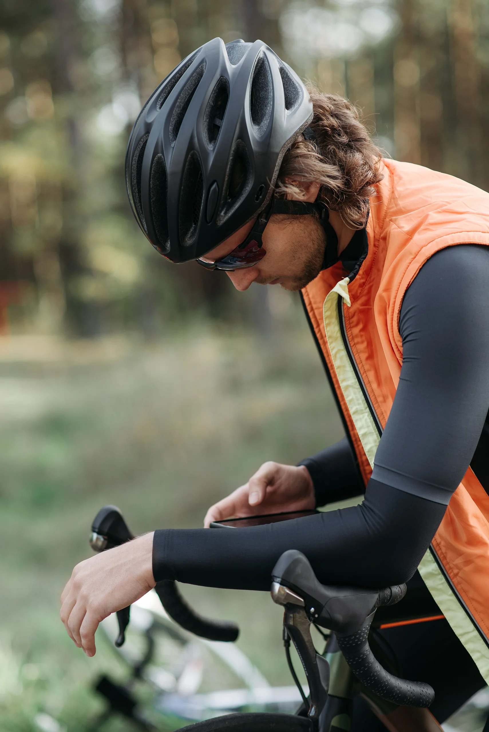 Cykelrytter i skoven tjekker træningsplanen på mobilen - Coach Lykke Endurance Landevejscykelrytter i orange vest holder pause i skoven og tjekker dagens træningspas i træningsappen på mobilen
