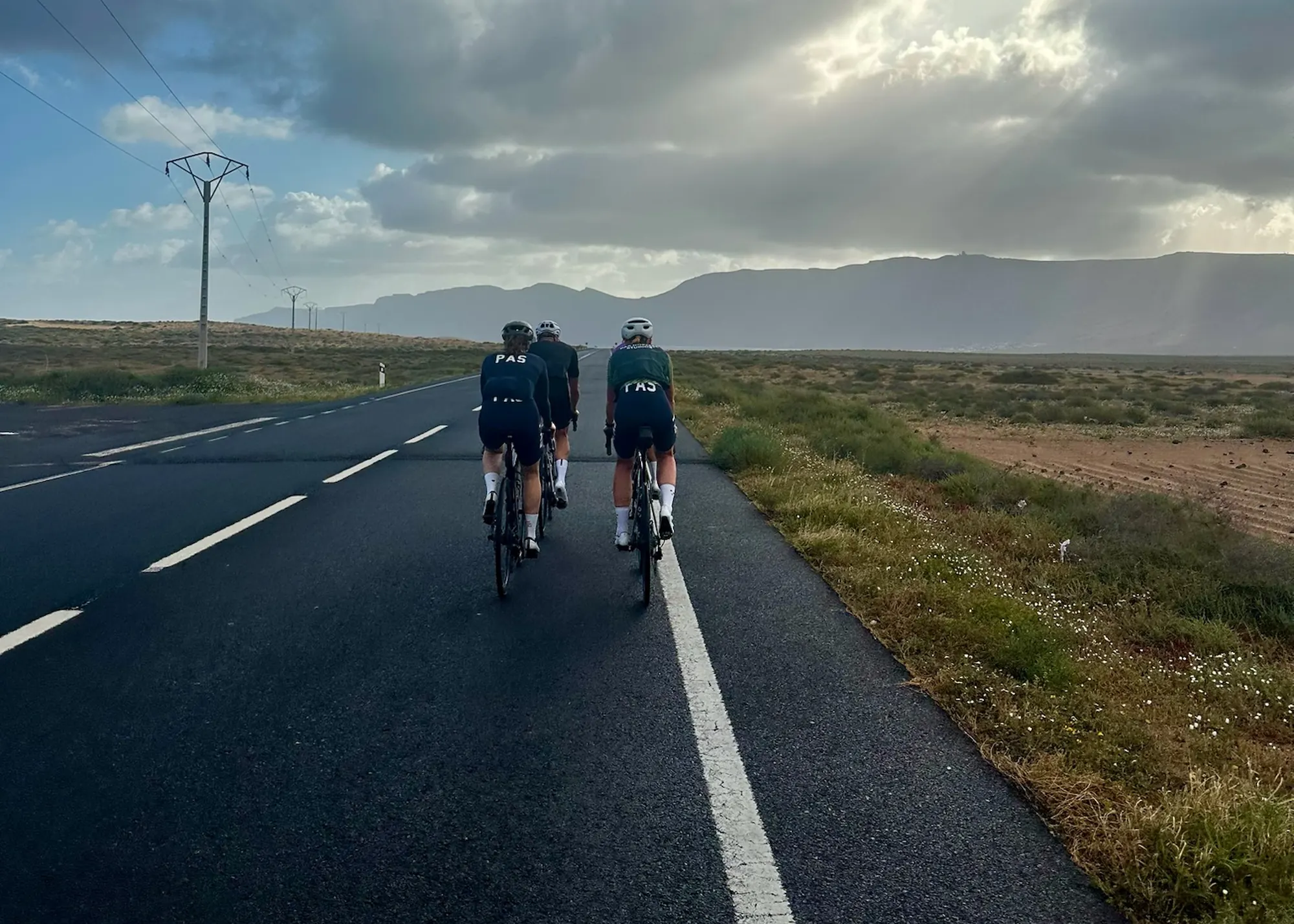Cykelryttere under en dramatisk himmel - Coach Lykke Endurance Tre cykelryttere på landevej under dramatisk himmel på træningslejr med cykeltræner Thomas Lykke