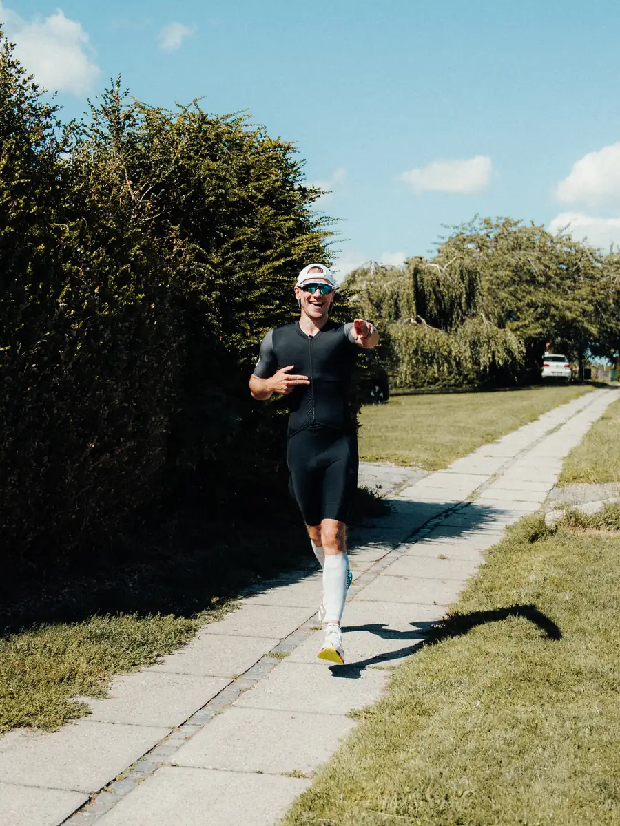Løbeprogram – løber på sti i sommersol - Coach Lykke Endurance Smilende løber i trisuit på en sti i sommersol – personligt løbeprogram