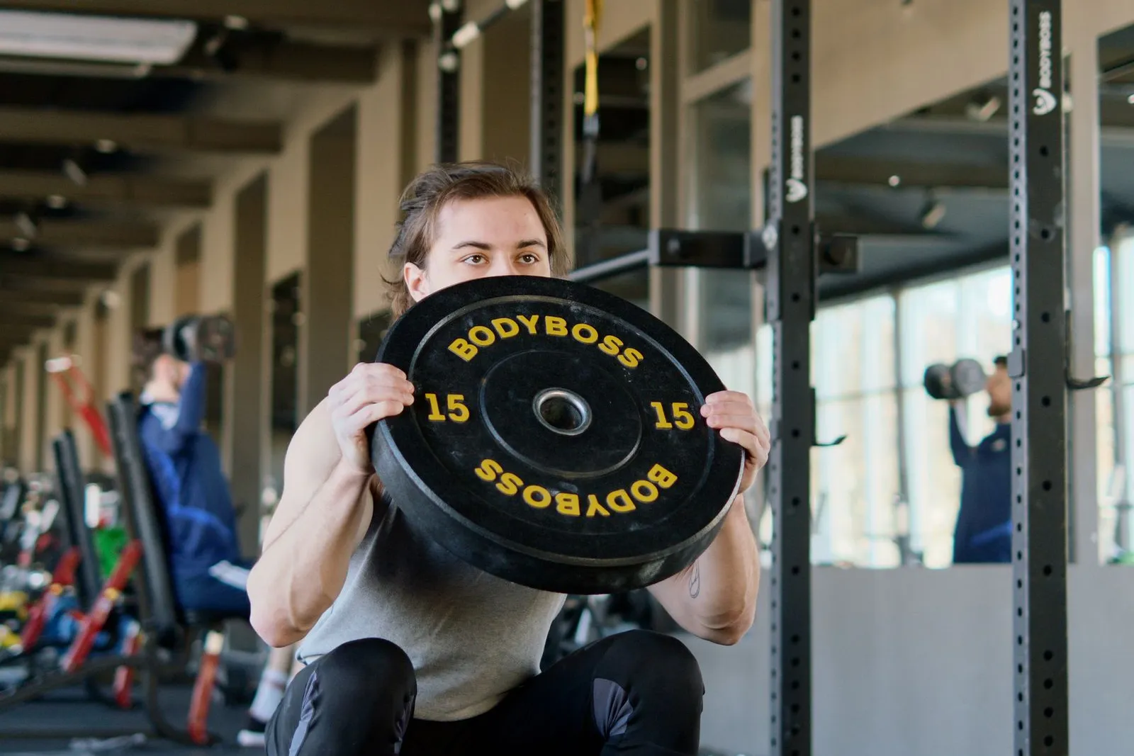 Styrketræning for cykelryttere: ung mand i squat med 15 kg vægtskive holdt foran brystet i et styrkerack