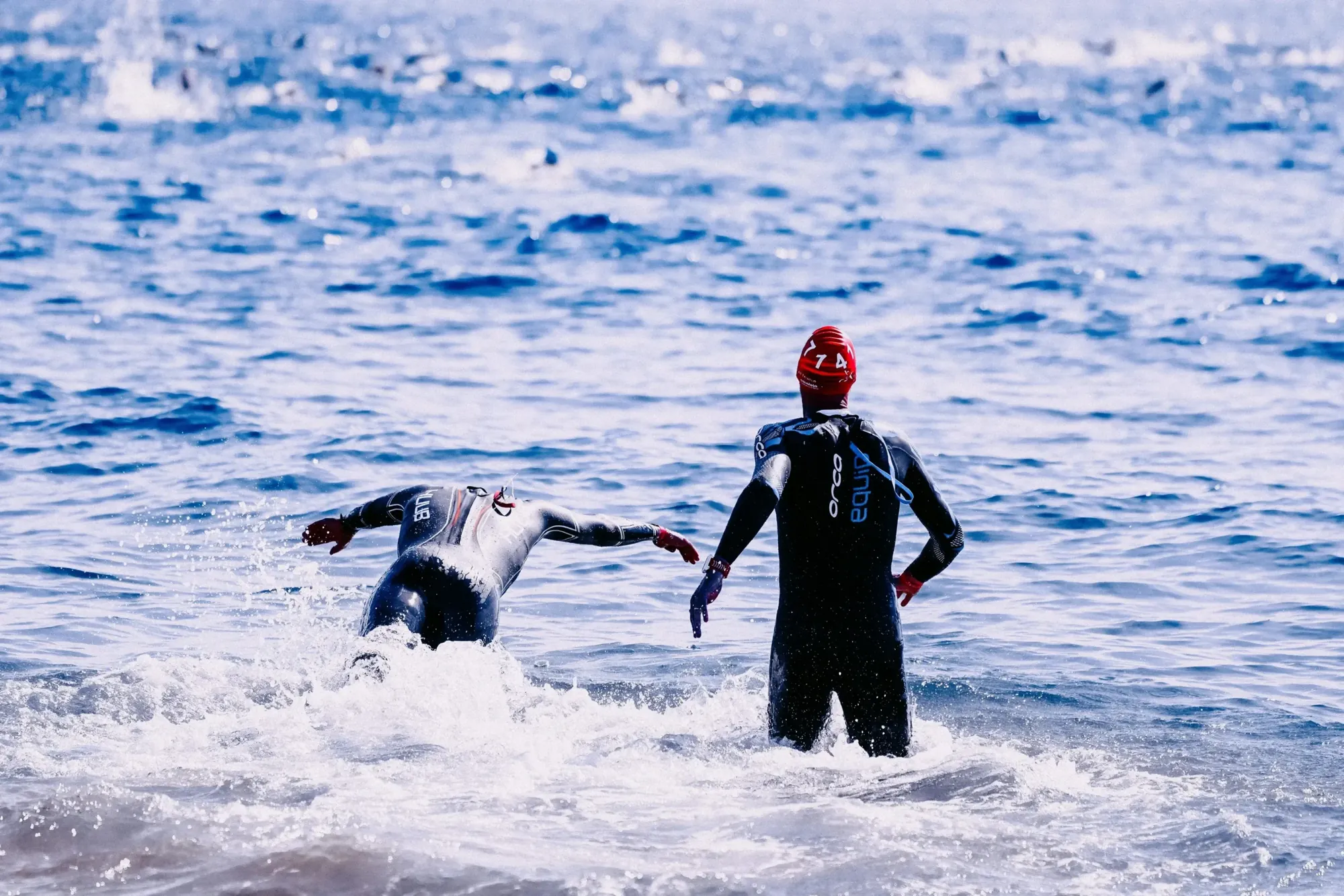 Træningszoner triatlon: open water-start - Coach Lykke Endurance To triatleter i våddragt vader ud i havet – træningszoner i triatlon starter med svømningen