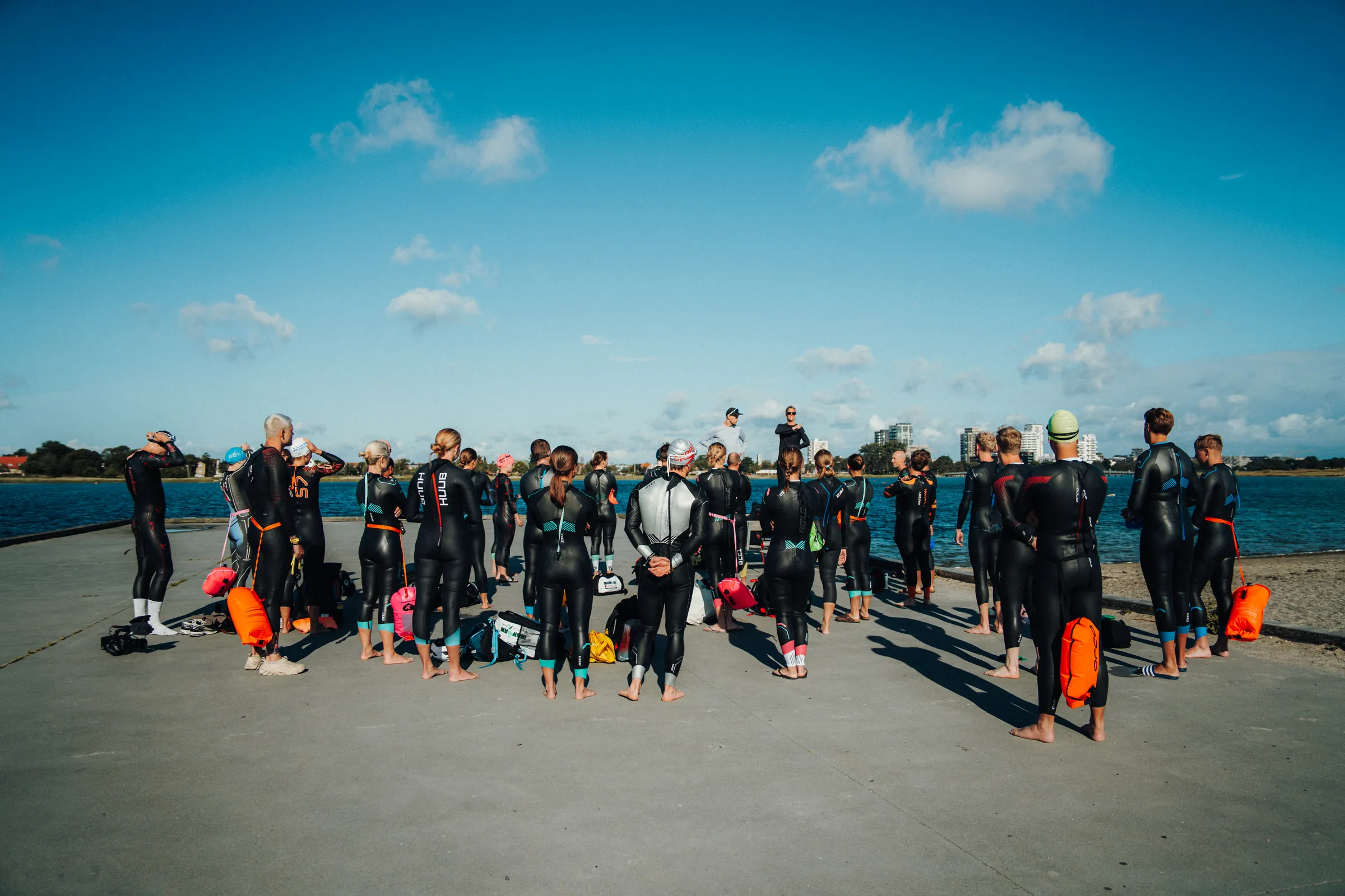 Triatlon træningsprogram: triatleter i våddragt på mole - Coach Lykke Endurance Triatleter i våddragter samlet på en mole ved vandet før en åbent vand-svømmetræning