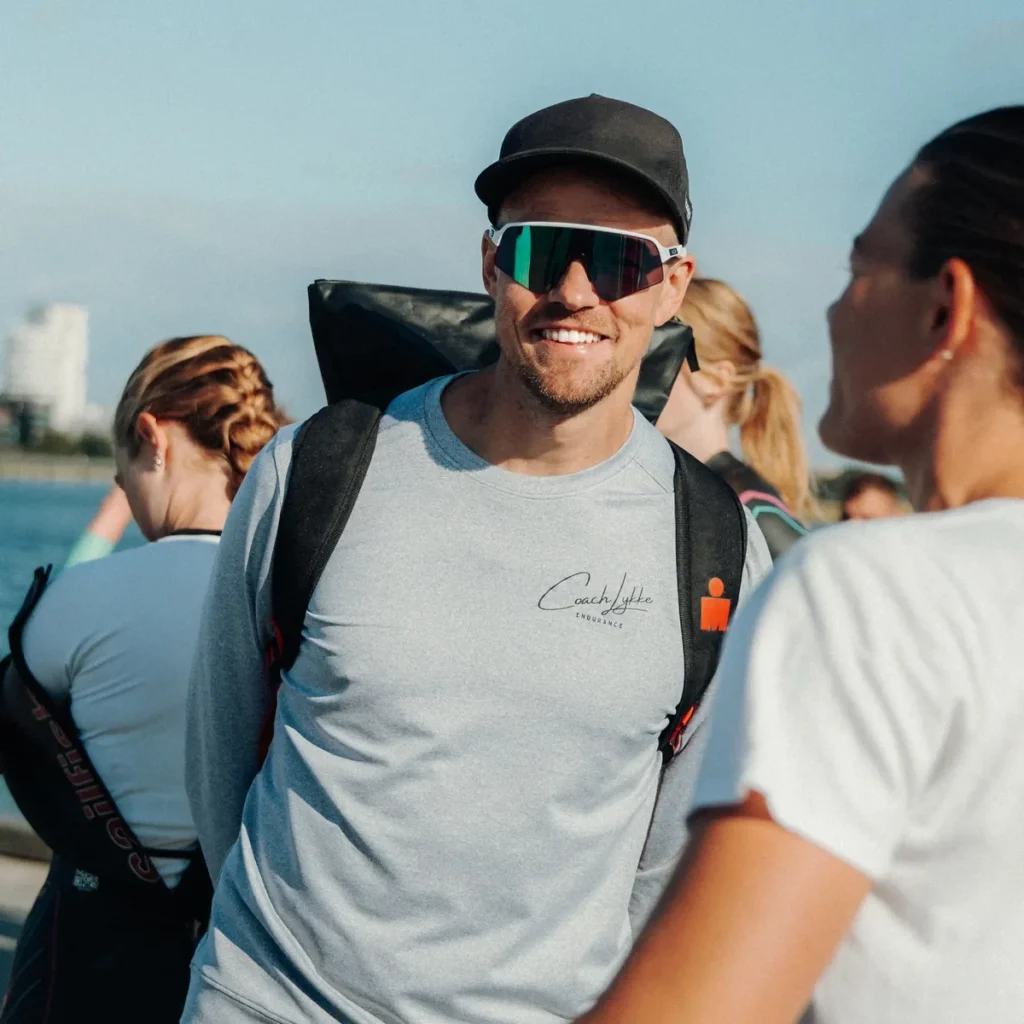 Thomas Lykke Sørensen sammen med sine atleter - Coach Lykke Endurance Thomas Lykke Sørensen i grå sweater sammen med atleter ved vandet før svømmetræning